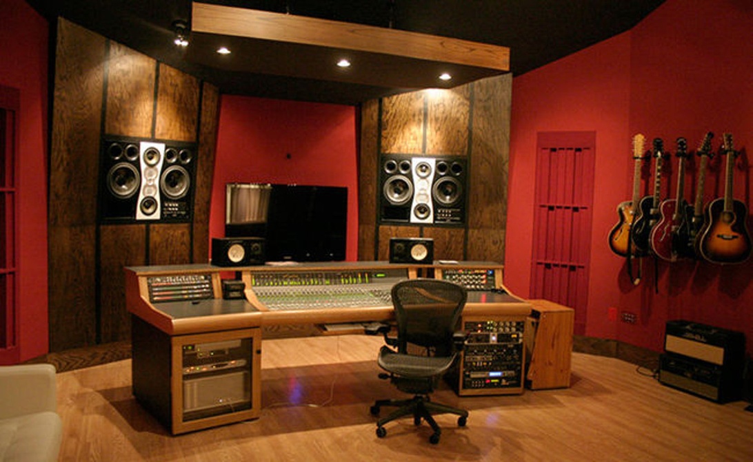 En musikstudio med röda väggar, mixerbord och flera gitarrer upphängda på väggen, vilket signalerar en miljö specialiserad på musikproduktion.